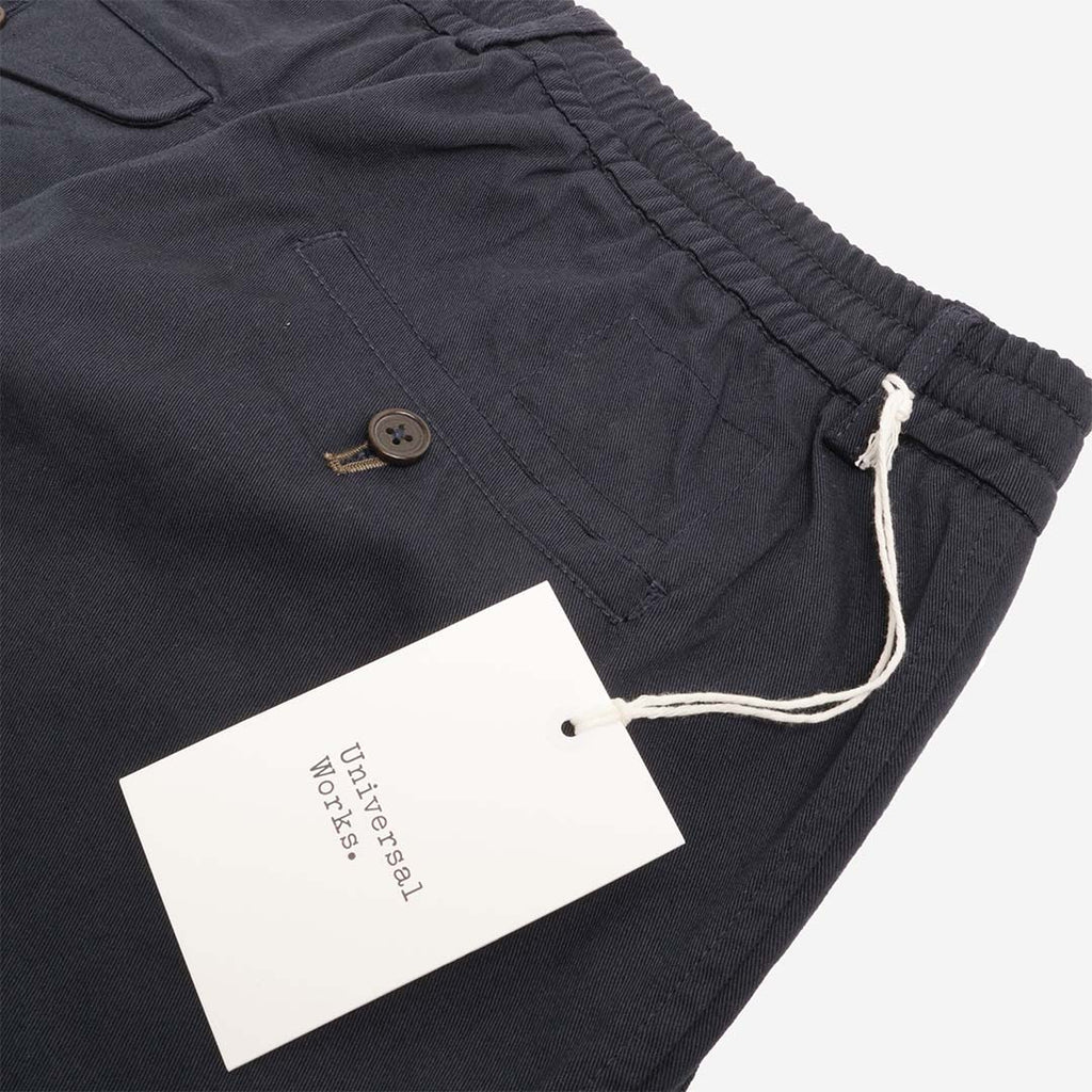 Universal Works branded hang tag on navy trousers